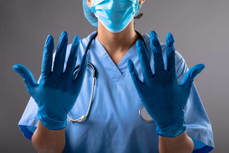 Mid section of female surgeon wearing surgical gloves against grey background. healthcare and medical professionalism conceptの写真素材