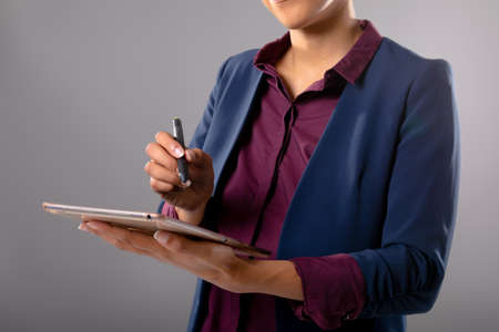 Mid section of businesswoman using graphic tablet against grey background. business, professionalism...