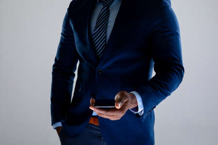 Mid section of african american businessman holding smartphone against grey background. business, professionalism and technology conceptの写真素材