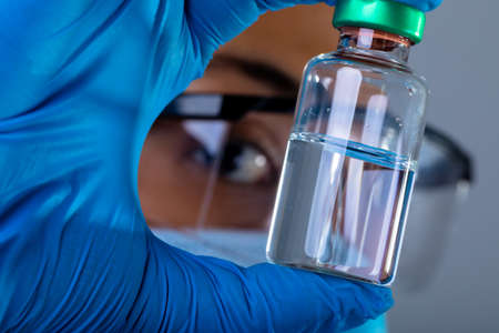Close up of female surgeon holding covid-19 vaccine bottle against grey background. vaccination for prevention of coronavirus outbreak conceptの写真素材