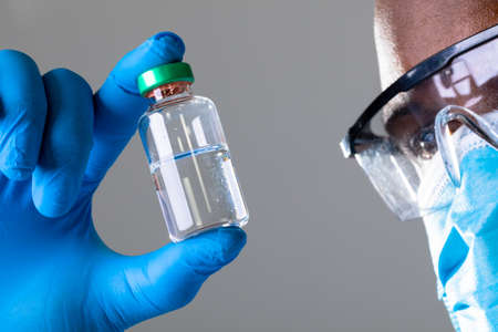Close up of african american male health worker wearing face mask holding covid-19 vaccine bottle....