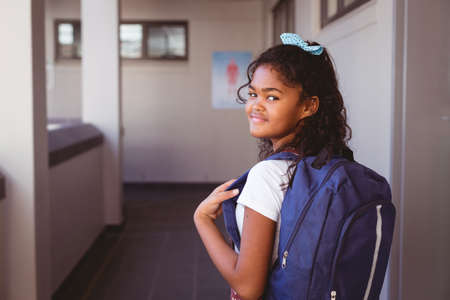Portrait of smiling african american schoolgirl standing in school corridor wearing schoolbag. childhood and education at elementary school.の写真素材