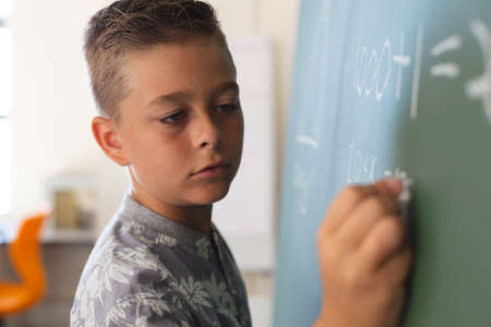 Caucasian boy standing at chalkboard writing in classroom during maths lesson. childhood and education at elementary school.の写真素材