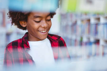 Laughing african american schoolboy reading book standing in school library. childhood and education...