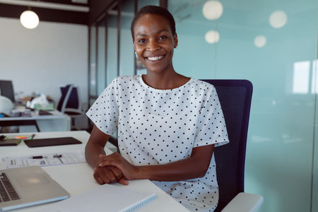 Smiling african american businesswoman sitting at desk at work. independent creative business at a...