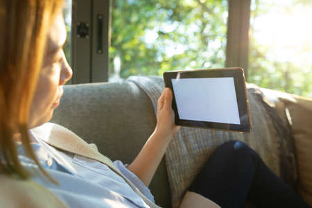 Asian woman using tablet with blank screen, sitting on sofa at home. at home in isolation during quarantine lockdown.の写真素材