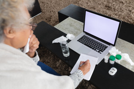 Mixed race senior woman sitting on sofa making video call using laptop. staying at home in isolation during quarantine lockdown.の写真素材