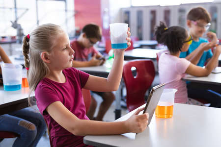 Caucasian boy holding a beaker and digital tablet in science class at laboratory. school and education conceptの写真素材