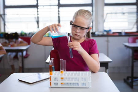 Caucasian girl pouring chemical from beaker into test tube in science class at laboratory. school...