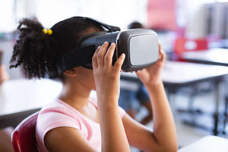 African american girl wearing vr headset while sitting on her desk in the class at school. school and education conceptの写真素材