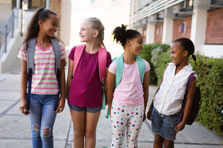 Group of diverse female students with backpacks smiling while looking at each other at school. school and education conceptの写真素材