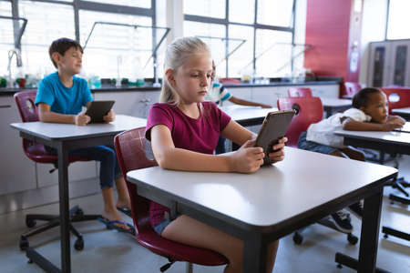 Caucasian girl using digital tablet while sitting on her desk in the class at school. school and education conceptの写真素材