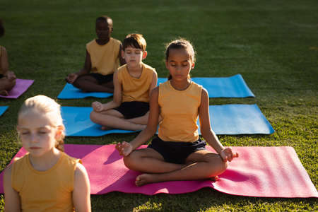Group of diverse students practicing yoga and meditating sitting on yoga mats in garden at school. school and education conceptの写真素材