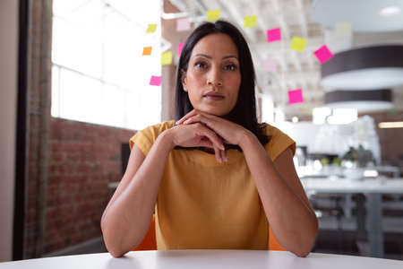 Serious caucasian businesswoman sitting at desk leaning chin on hands, listening during a video...