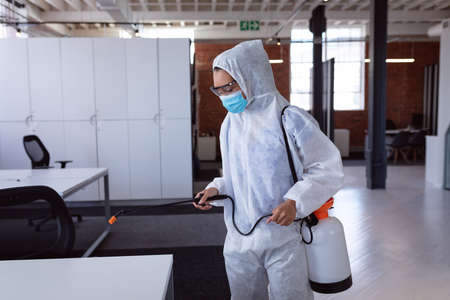 Cleaner wearing ppe suit, glasses and mask disinfecting office workspace.の写真素材