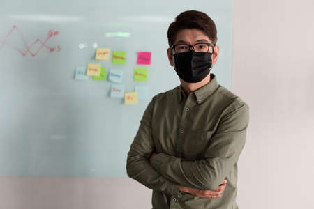 Portrait of asian businessman wearing face mask standing in meeting room looking to camera.の写真素材