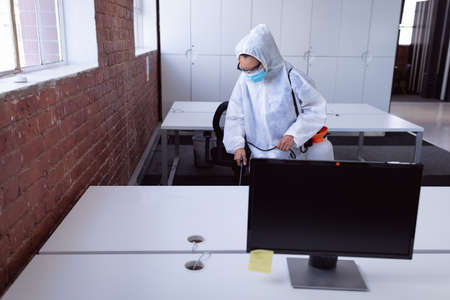 Cleaner wearing ppe suit, glasses and mask disinfecting office workspaceの写真素材