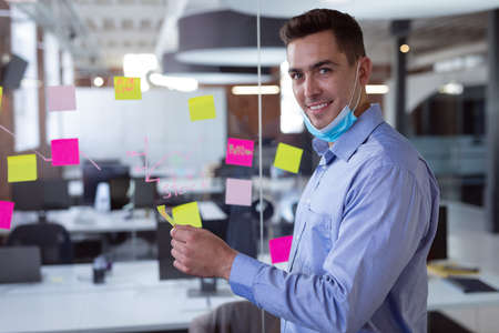 Portrait of caucasian businessman in lowered face mask brainstorming, smiling to camera.