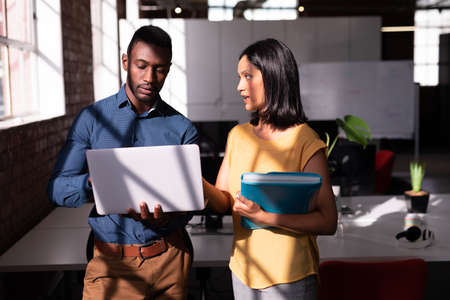 Serious diverse male and female colleague standing in office discussing, looking at laptop together. working in business at a modern office.の写真素材