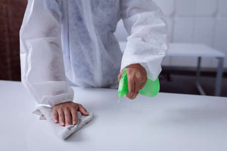 Midsection of cleaner wearing ppe suit disinfecting office workspace, wiping desks. hygiene in...