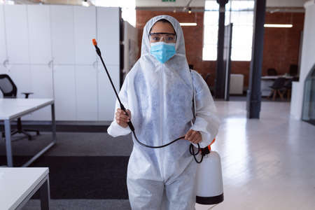 Portrait of cleaner wearing ppe suit, glasses and mask disinfecting office workspace. hygiene in business at a modern office during pandemic.の写真素材