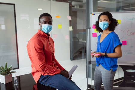 Portrait of diverse male and female colleague in face masks brainstorming in office. working in business at a modern office during coronavirus covid 19 pandemic. .の写真素材