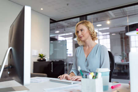 Smiling caucasian businesswoman sitting at desk in office using computer. working in business at a modern office.の写真素材