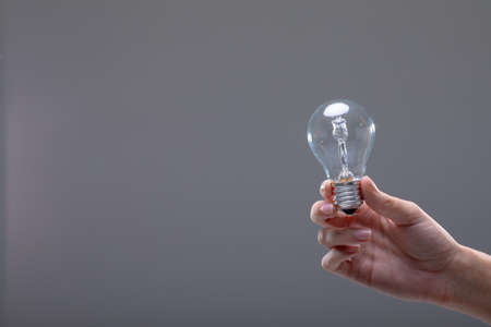 Close up of caucasian businesswoman holding light bulb, isolated on grey background. business, technology, communication and growth concept.の写真素材