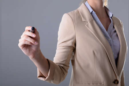 Midsection of caucasian businesswoman holding pen, isolated on grey background. business, technology, communication and growth concept.の写真素材