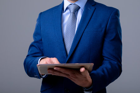 Midsection of caucasian businessman using digital tablet, isolated on grey background. business technology, communication and growth concept.の写真素材