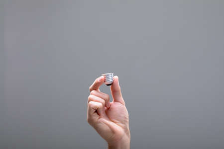 Close up of caucasian businessman holding base of light bulb, isolated on grey background. business...