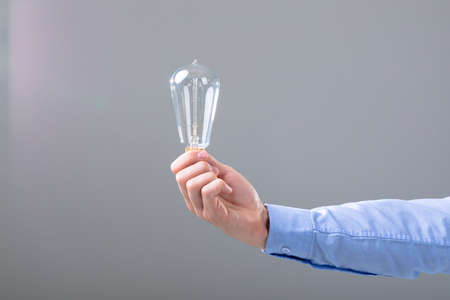 Midsection of caucasian businessman holding light bulb, isolated on grey background. business...