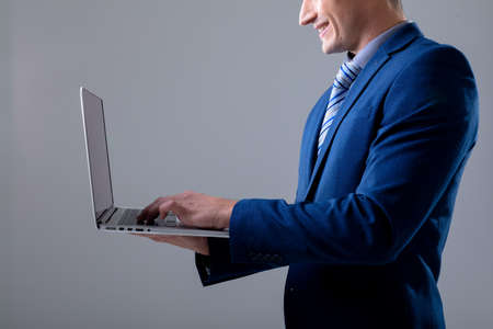 Smiling caucasian businessman using laptop, isolated on grey background. business technology,...
