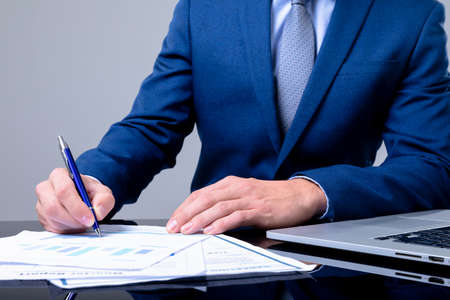Midsection of caucasian businessman using laptop and taking notes, isolated on grey background....