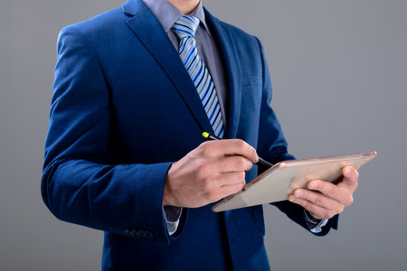 Midsection of caucasian businessman using tablet, isolated on grey background. business technology, communication and growth concept.の写真素材