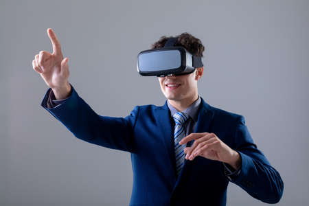 Caucasian businessman wearing vr headset touching virtual interface, isolated on grey background. business technology, communication and growth concept digitally generated composite image.の写真素材