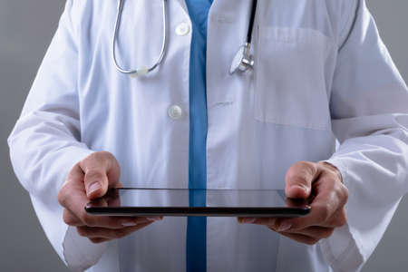 Midsection of caucasian male doctor using tablet, isolated on grey background. medical and...
