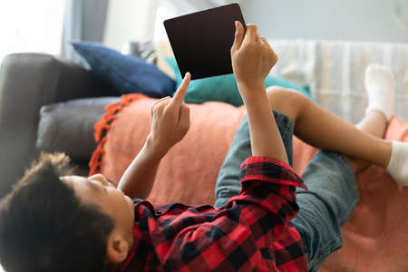 Asian boy using tablet with blank screen lying on floor at home. domestic lifestyle, leisure and technology during  pandemic concept.の写真素材