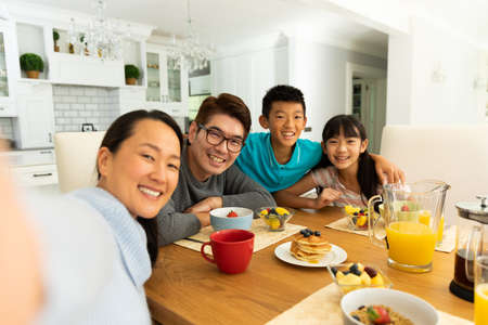 Asian couple with son and daughter sitting at table eating together at home. domestic lifestyle and leisure family time concept.の写真素材
