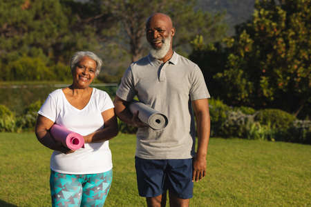 Portrait of smiling senior african american couple with yoga mat in countryside retreat. retirement...