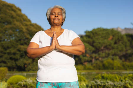 Senior african american woman with eyes closed practicing yoga in stunning countryside. retirement and active senior lifestyle concept.の写真素材