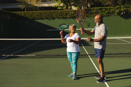 Portrait of smiling senior african american couple with tennis rackets on tennis court. retirement and active senior lifestyle concept.の写真素材