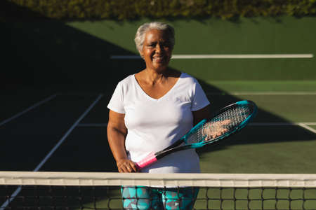 Portrait of smiling senior african american woman holding tennis racket on tennis court. retirement and active senior lifestyle concept.の写真素材