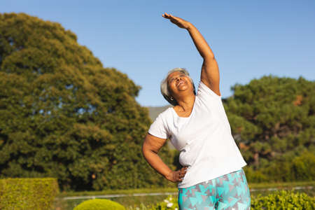 Senior smiling african american woman practicing yoga in stunning countryside. retirement and active...