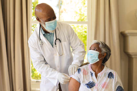 Senior african american woman and male doctor in face masks, woman receiving vaccination. retirement...