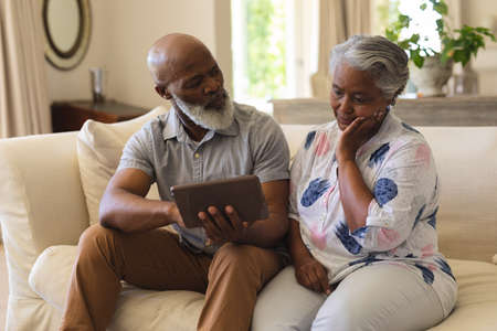 Senior african american couple sitting on sofa using tablet. retreat, retirement and happy senior lifestyle concept.の写真素材
