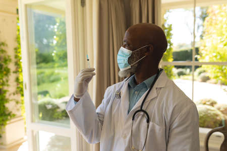 Senior african american male doctor in face mask preparing vaccination. retirement and senior lifestyle during covid 19 pandemic concept.の写真素材