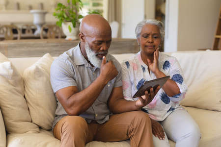 Senior african american couple sitting on sofa using tablet. retreat, retirement and happy senior lifestyle concept.の写真素材