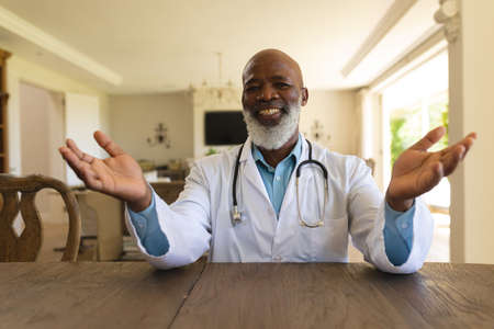 Portrait of smiling senior african american male doctor in lab coat during video consultation....