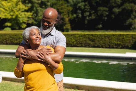 Senior african american couple spending time in sunny garden together embracing and smiling....